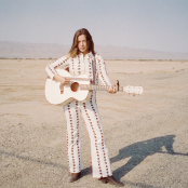 Artist Jade Bird standing with guitar in desert